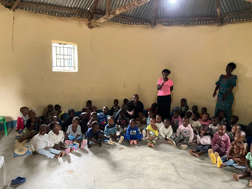 Children seated on a classroom floor with two adults nearby