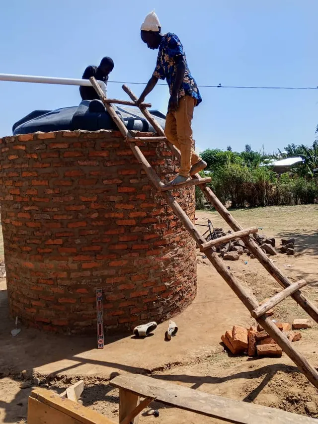Two workers beside a water tank, one standing on a wooden ladder